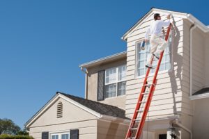 columbia paint House painter with paint brush painting the trim of a 2nd story window of a Cape Cod Style house.